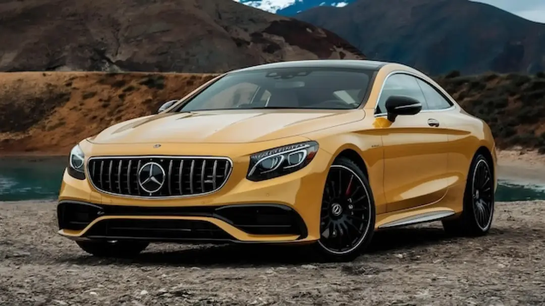 Yellow Mercedes-Benz S-Class coupe parked on gravel by mountains